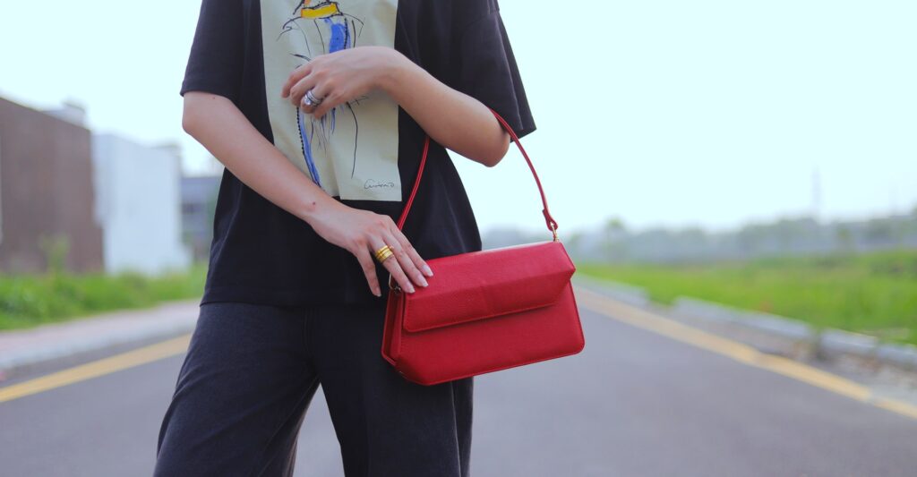 A girl wearing Black Trouser shirt is holding a sling bag on her hands .